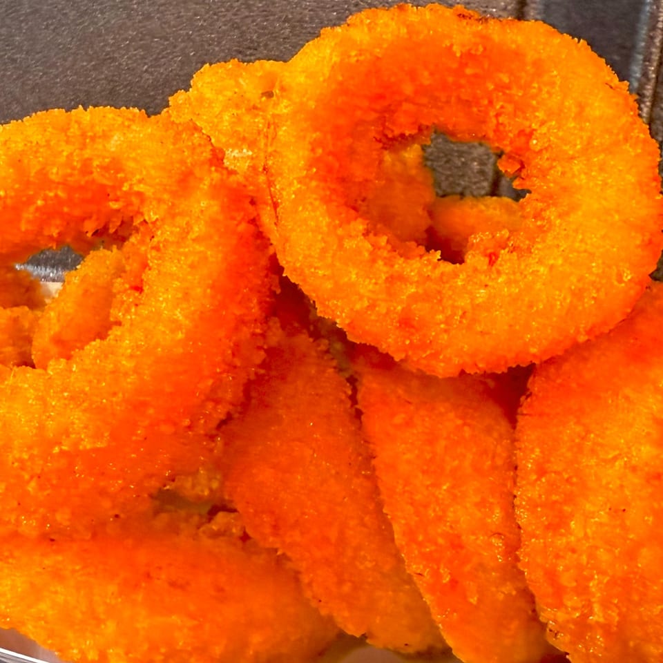 Close-up of several golden-orange, breaded onion rings from Duke's Grill, ready to be eaten.
