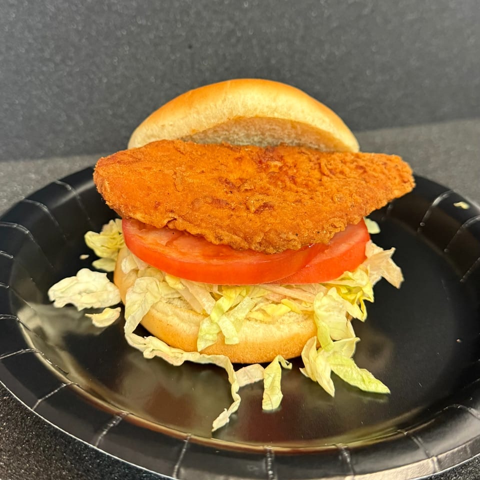 Duke's Grill crispy chicken sandwich with lettuce and tomato on a black plate.