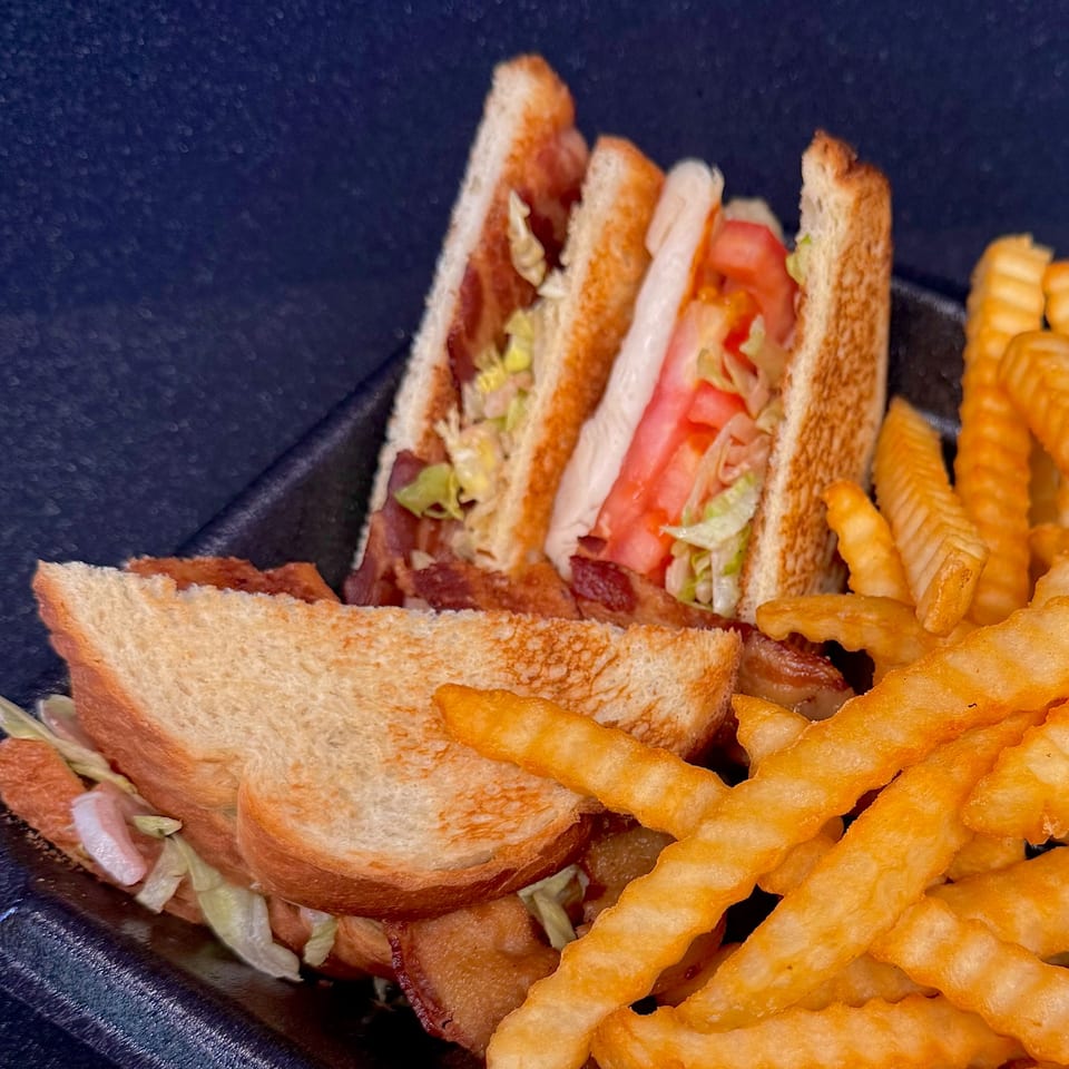 A Duke's Grill club sandwich with bacon, lettuce, and tomato, served with crinkle-cut fries.